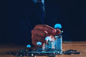 Pessoa a interagir com gráficos financeiros digitais sobre pilhas de moedas, simbolizando o crescimento dos investimentos e a gestão de património.