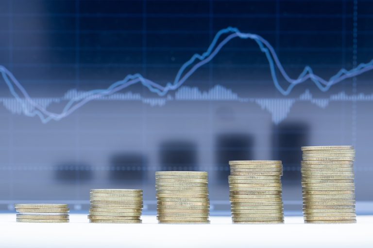 Pilhas de moedas de altura crescente, com gráficos financeiros em segundo plano, simbolizando o crescimento da poupança e a evolução das taxas de juro.